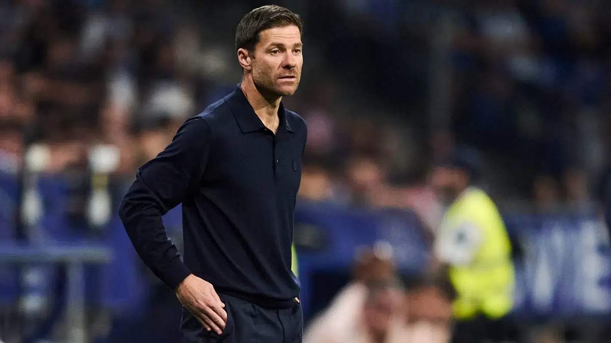 Xabi Alonso sitting on the Real Madrid bench during a match, focused and tense, highlighting the pressure of coaching.