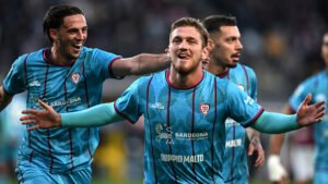 Semih Kılıçsoy celebrates a goal in Cagliari colours with the crowd blurred behind him
